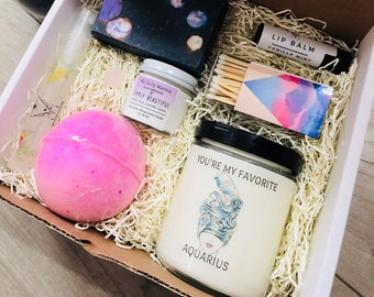 May include: A gift box filled with a variety of self-care items, including a bath bomb, a candle, a lip balm, matches, and a bar of soap. The candle has the text "You're My Favorite Aquarius" on the front.