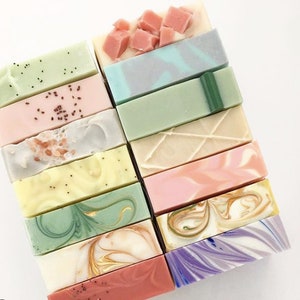 May include: A stack of 15 handmade soap bars in various colors and patterns, including green, pink, purple, and white. The soaps have different textures and designs, such as swirls, speckles, and stripes.