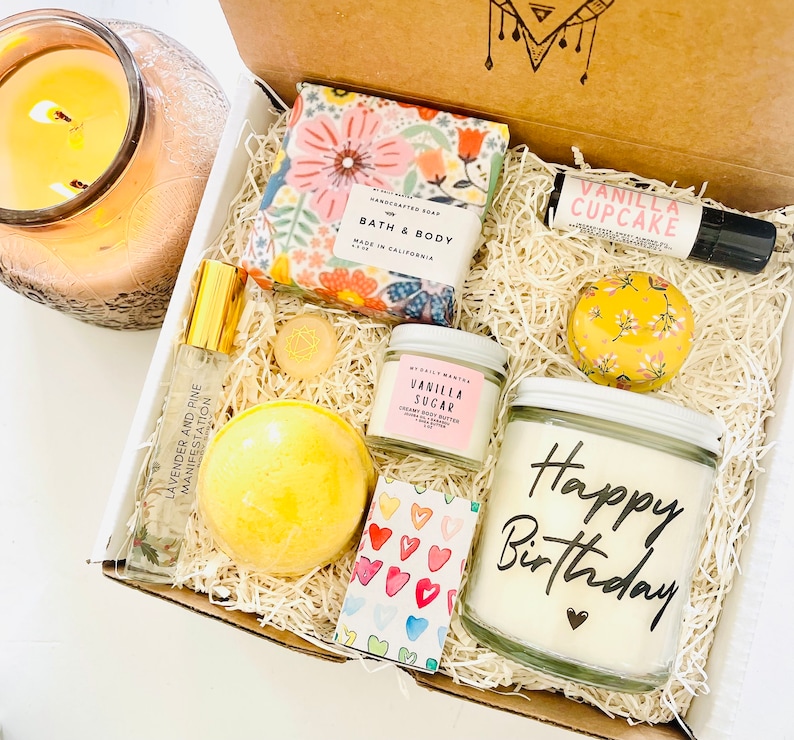 May include: A gift box filled with a variety of items, including a bath and body soap, a candle, a bath bomb, a body butter, and a small bottle of essential oil. The box is decorated with a floral pattern and the words "Happy Birthday".