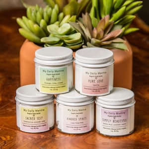 May include: Five white jars of organic body butter with different scents and names. The jars are labeled "My Daily Mantra" and each has a different scent and name: "Happiness", "Pure Love", "Sacred Self", "Kindred Spirits", and "Simply Beautiful".