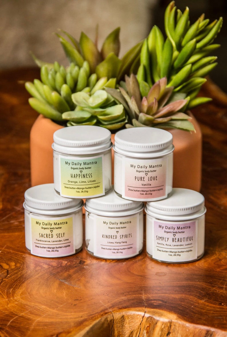 May include: Five white jars of organic body butter with different scents and names. The jars are labeled "My Daily Mantra" and each has a different scent and name: "Happiness", "Pure Love", "Sacred Self", "Kindred Spirits", and "Simply Beautiful".