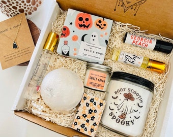 May include: A gift box containing a ghost necklace on a card, a pumpkin and ghost soap bar, a Georgia Peach lip balm, a Hey Boo roller perfume, a white bath bomb, a Sweet Cream body butter jar, and a Boot Scootin Spooky candle with a ghost.