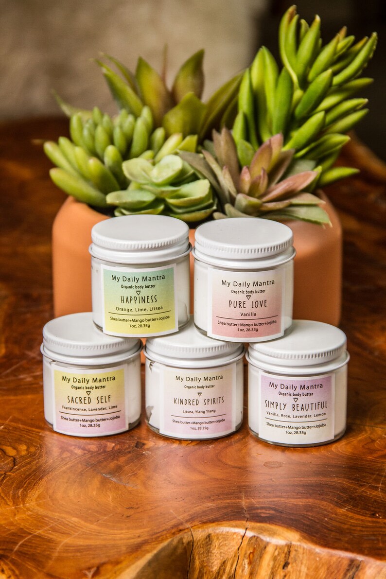 May include: Five white jars of organic body butter with pink labels and white lids. The labels have the text "My Daily Mantra" and the name of each scent: "Happiness", "Pure Love", "Sacred Self", "Kindred Spirits", and "Simply Beautiful".