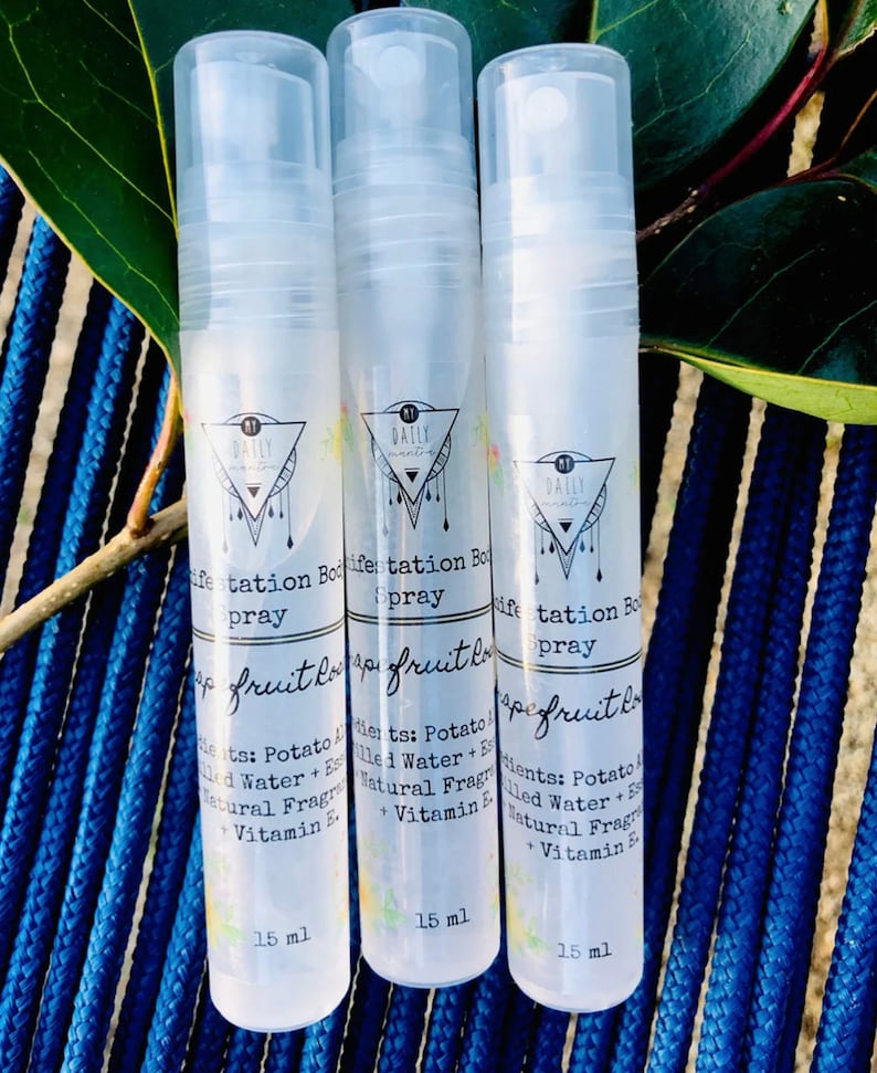 May include: Three clear plastic bottles with a white label and black text. The label has a triangle with a circle inside. The text on the label reads "Daily Manifestation Body Spray" and "Grapefruit Love". The bottles are 15 ml each.