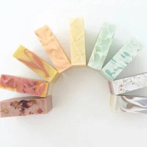 May include: A collection of ten handmade soap bars in various colors and patterns, arranged in a semi-circle. The soaps are made with natural ingredients and are perfect for a variety of skin types.