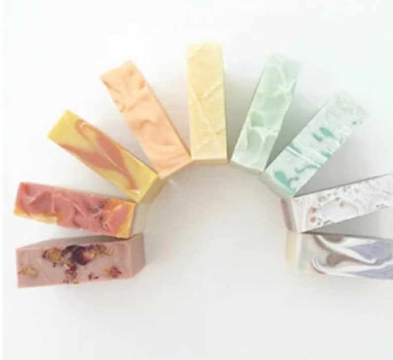 May include: A collection of ten handmade soap bars in various colors and patterns, arranged in a semi-circle. The soaps are made with natural ingredients and are perfect for a variety of skin types.