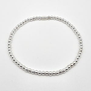 May include: A silver beaded bracelet with small, round beads. The bracelet is strung together with a silver clasp. The beads are evenly spaced and reflect light, creating a shiny appearance. The bracelet is shown against a white background.