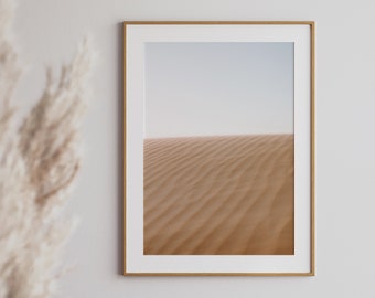 May include: A framed photograph of a desert landscape with sand dunes in shades of beige and brown. The sky is a light blue and the horizon is visible in the distance.