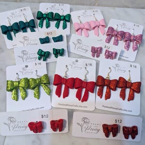 May include: A collection of bow-shaped earrings in various colors, including green, pink, red, and glittery options. Some earrings are on cards with the text "Pearl and Peony Crafts.etsy.com" and prices of $12 and $16.