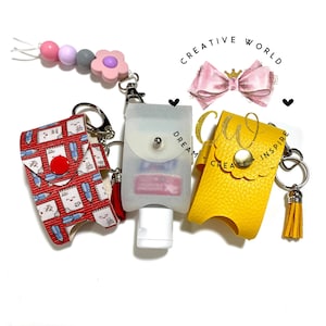 以下が含まれることがあります： キーチェーン付きのハンドサニタイザーホルダーが3つあります。1つ目は白と青の模様の赤いもの、2つ目は透明なプラスチック製、3つ目は黄色の革製です。キーチェーンにはタッセルとチャームが付いています。