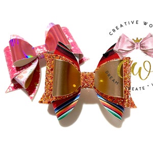 May include: Two hair bows, one with a red, orange, and yellow striped pattern and gold glitter, and the other with a pink and white iridescent pattern. The bow with the striped pattern has a gold mirror in the center. The bows are on a white background.