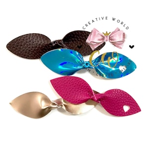 May include: A selection of handmade hair bows in different colours and textures. The bows include a textured brown leather bow, a teal iridescent bow, a pink bow, and a gold and magenta bow. The bows are arranged on a white background.