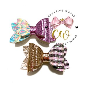 May include: Two handmade hair bows. One bow is pink with glitter and white stripes. The other bow is a gold color with a textured finish. Both bows are tied with a knot in the center.