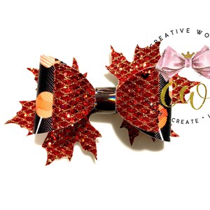 May include: A red and black glitter maple leaf hair bow with gold accents. The bow is attached to a silver alligator clip.