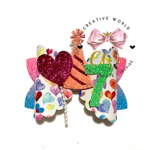 May include: A colorful hair bow with a heart, party hat, and the number 7. The bow is decorated with a white background with colorful hearts and a pearl strand.