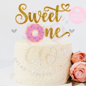 May include: Gold glitter cake topper with the words "Sweet One" and a pink donut with sprinkles.