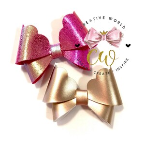 May include: Two handmade hair bows with scalloped edges. The bow on the left is pink with a gold shimmer, and the bow on the right is gold with a pink shimmer.