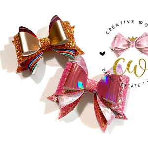 May include: Two handmade hair bows, one with a rainbow and gold glitter design and the other with pink and iridescent glitter. The bows are on a white background with a logo that says "Creative World" and "Dream, Create, Inspire".