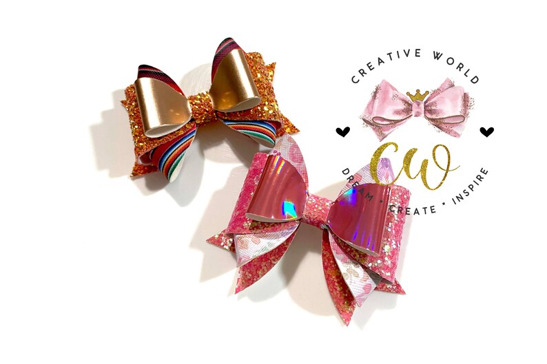 May include: Two handmade hair bows, one with a rainbow and gold glitter design and the other with pink and iridescent glitter. The bows are on a white background with a logo that says "Creative World" and "Dream, Create, Inspire".