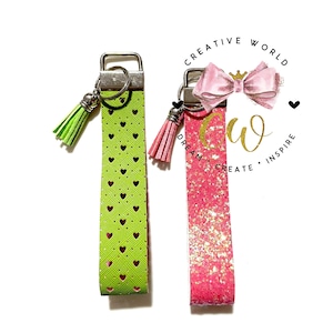 May include: Two keychains with silver key rings and tassels. One keychain is green with a heart pattern and the other is pink with glitter. The keychains are labeled "Creative World Dream Create Inspire".