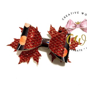 May include: A red and black glitter bow with a maple leaf design. The bow is tied with a black ribbon and has a gold glitter accent.