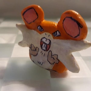 May include: A hand-painted figurine of a Pokémon character with orange and white fur. The character has a wide open mouth with sharp teeth and is making a fierce expression. The figurine is made of clay and has a textured surface.