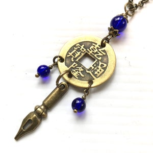 May include: A gold-toned necklace with a round coin pendant featuring Chinese characters. The pendant is accented with three dangling blue glass beads and a small, antique-style pen charm.