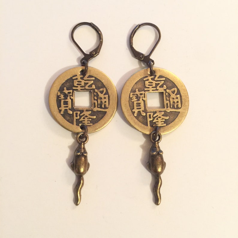 May include: A pair of gold-tone earrings featuring a round coin charm with Chinese characters and a dangling rat charm.