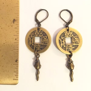 May include: A pair of gold-tone earrings featuring a Chinese coin charm with the characters "福" (f&uacute;) and "財" (c&aacute;i) meaning "fortune" and "wealth" respectively, and a small dangling rat charm.