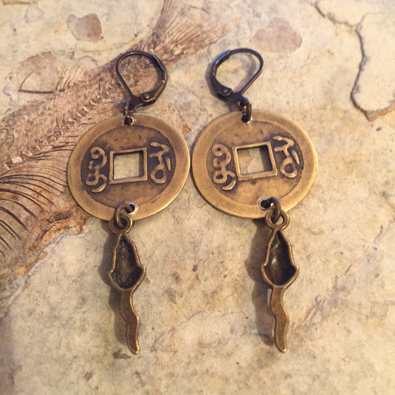 May include: Brass earrings with a round coin design featuring Chinese characters and a dangling charm in the shape of a stylized fish.