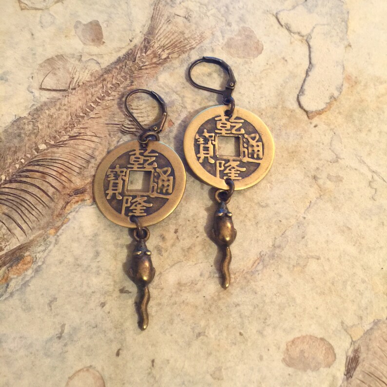 May include: Brass earrings with a Chinese coin charm and a dangling rat charm. The coin has Chinese characters that read "Prosperity and Treasure".