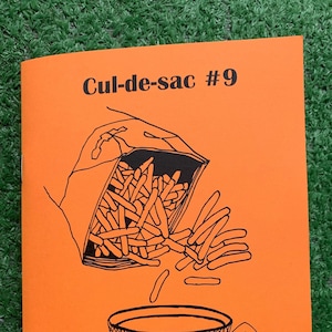 May include: An orange cover of a magazine called "Cul-de-sac #9" with a black and white illustration of a bag of french fries spilling out onto a teacup and saucer. The text "The Food Issue" is printed in black at the bottom of the cover.