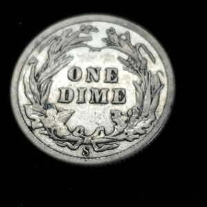 Peut inclure: Une pi&egrave;ce de monnaie am&eacute;ricaine en argent d'une valeur de dix cents avec l'inscription "ONE DIME" entour&eacute;e d'une couronne de feuilles. La pi&egrave;ce porte une petite marque de fabrique "S".