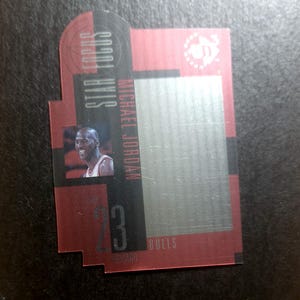 May include: A red and black trading card featuring a photo of Michael Jordan, a basketball player for the Chicago Bulls. The card has the text "Michael Jordan" and "Scottie Pippen" on the left side and "23" and "Bulls" on the bottom right side.