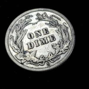 Peut inclure: Une pi&egrave;ce de monnaie am&eacute;ricaine en argent d'une valeur de dix cents, avec les mots "ONE DIME" entour&eacute;s d'une couronne de feuilles et la lettre "S" en bas.