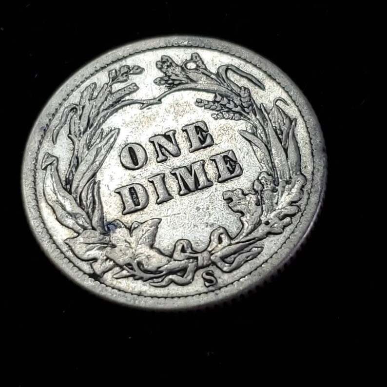 Peut inclure: Une pi&egrave;ce de monnaie am&eacute;ricaine en argent d'une valeur de dix cents, avec les mots "ONE DIME" entour&eacute;s d'une couronne de feuilles et la lettre "S" en bas.