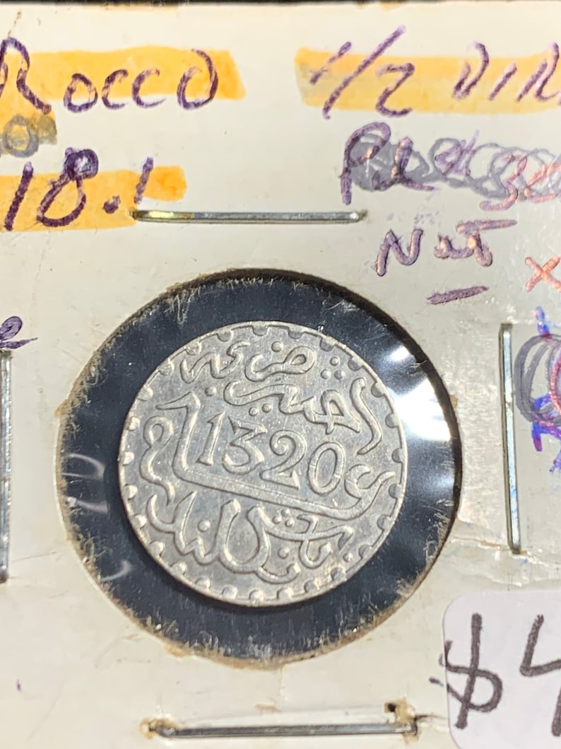 Puede incluir: Una moneda de plata con escritura &aacute;rabe y la fecha 11320c. La moneda est&aacute; en un soporte de moneda de pl&aacute;stico con fondo blanco.