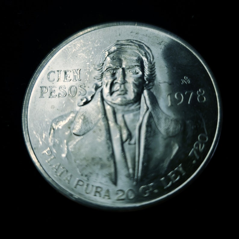 Op de afbeelding: Een zilveren munt met de tekst "CIEN PESOS" en het jaartal "1978". De munt toont een portret van een man en de woorden "PLATA PURA 20 G. LEY .720". De munt is rond en heeft een gedetailleerd ontwerp.