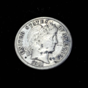 Peut inclure: Pi&egrave;ce de monnaie am&eacute;ricaine en argent de dix cents avec les mots "United States of America" et l'ann&eacute;e "1911" inscrits sur le bord. La pi&egrave;ce repr&eacute;sente un portrait de la Libert&eacute; avec une couronne de feuilles de laurier.