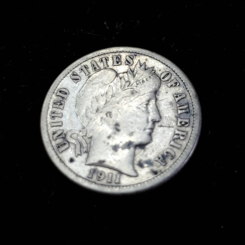 Peut inclure: Pi&egrave;ce de monnaie am&eacute;ricaine en argent de dix cents avec les mots "United States of America" et l'ann&eacute;e "1911" inscrits sur le bord. La pi&egrave;ce repr&eacute;sente un portrait de la Libert&eacute; avec une couronne de feuilles de laurier.