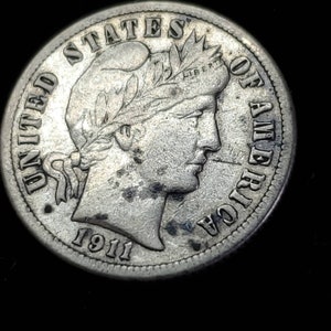 Peut inclure: Une pi&egrave;ce de monnaie am&eacute;ricaine en argent de dix cents avec l'ann&eacute;e 1911 inscrite en bas. La pi&egrave;ce repr&eacute;sente un portrait de la Libert&eacute; avec une couronne de laurier sur la t&ecirc;te et les mots "UNITED STATES OF AMERICA" autour du bord.
