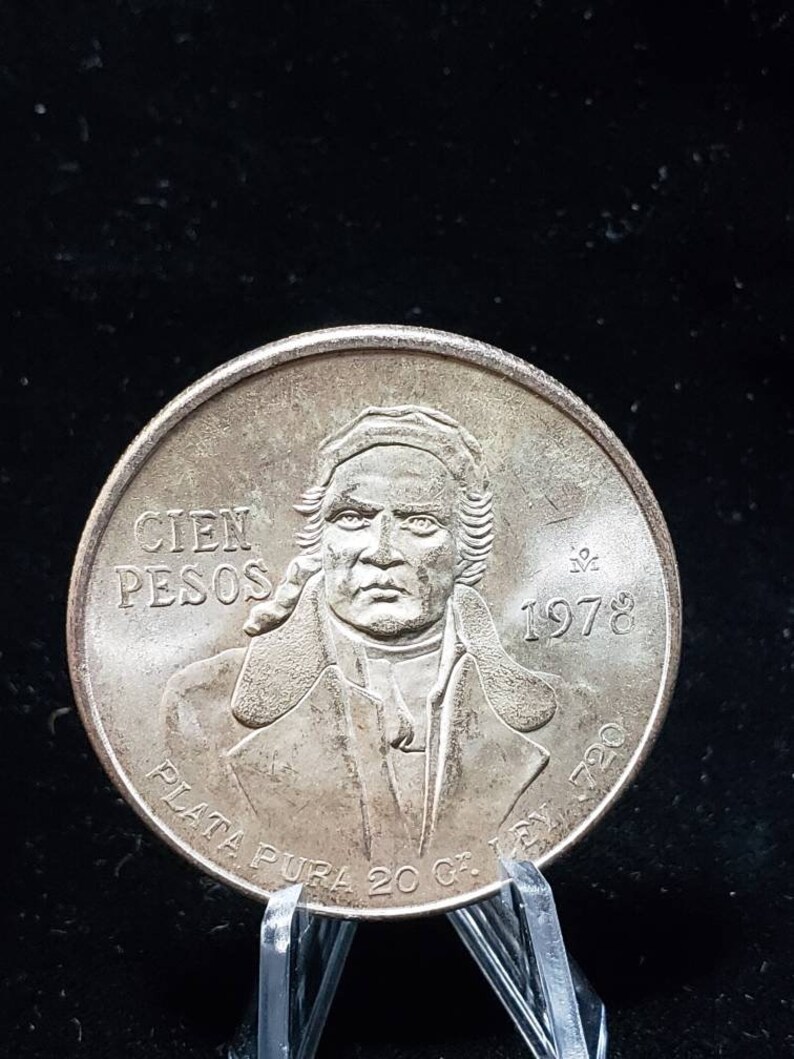 Op de afbeelding: Een zilveren munt met een portret van een man, met de tekst "CIEN PESOS" en het jaartal "1978". De munt heeft ook de tekst "PLATA PURA 20 G. LEY 720".