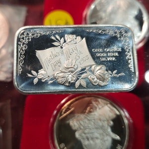 May include: A silver bar with an inscription that reads "Mother's Day 1973" and "One ounce .999 fine silver". The bar features a floral design with roses and leaves.