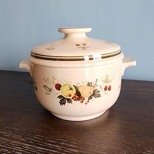 May include: A beige ceramic casserole dish with a lid. The dish has a floral design with apples, pears, and berries. The lid has a brown trim.