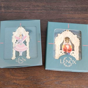 May include: Two Lenox Christmas ornaments in teal boxes. One features a ballerina with pink wings and a pink tutu. The other depicts a nutcracker soldier. Both are white with gold accents and the Lenox logo.