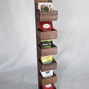 May include: Wooden wall-mounted tea bag organizer with five shelves. Each shelf holds a box of tea bags. The tea bags are labeled with the following flavors: Traditional Medicinals, Twinings Chai, Bigelow Green Tea, Bigelow Cozy Chamomile, and Celestial Seasonings Green Tea.