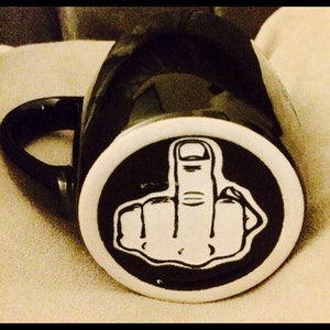 May include: Black coffee mug with a white circle and a white middle finger graphic.