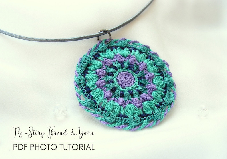 Op de afbeelding: Een gehaakte ketting met een hanger in teal, paars en donkerblauw met een mandala-ontwerp. De hanger is bevestigd aan een zilveren ketting.