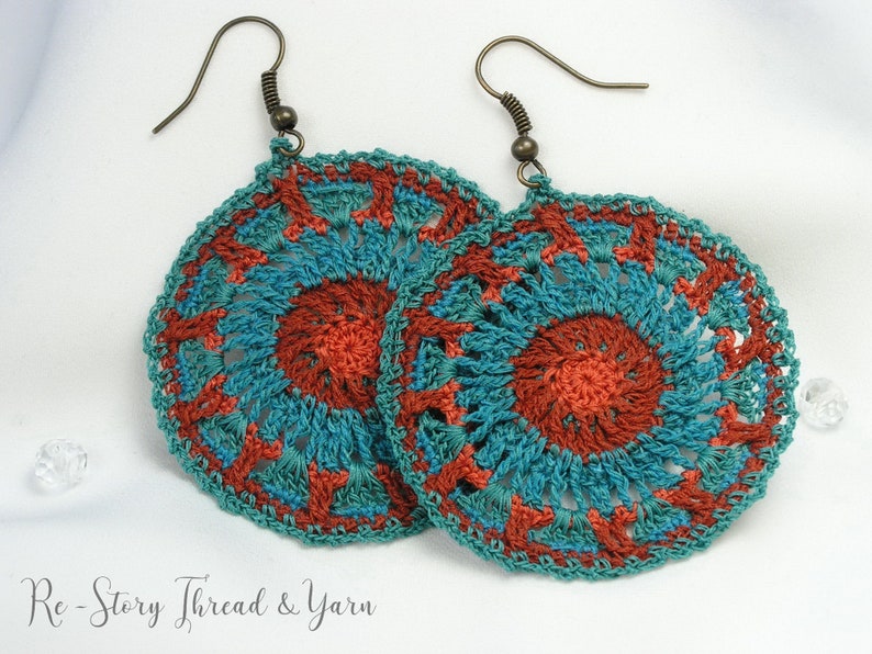 May include: A pair of crocheted earrings with a teal and orange mandala design. The earrings are made with a delicate, intricate pattern and have a bohemian style.