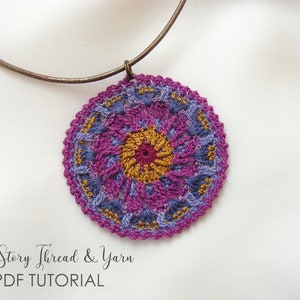 May include: A crocheted pendant necklace with a purple, blue, and gold mandala design. The necklace is made with a brown metal chain.